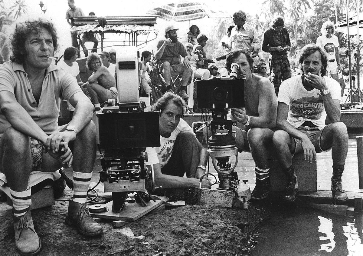 Storaro (kneeling at center) and his crew set up two cameras. Flanking him (from left) are camera assistant Rino Bernardini, operator Enrico Umetelli and camera assistant Mauro Marchetti. In the background, Coppola (seated) chats with AD Jerry Ziesmer (white shirt) as Dennis Hopper (in camo pants) stands by.