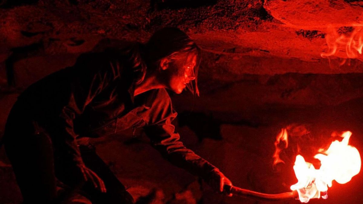 Sarah picks her way through a cavern, using a torch to light the way. 